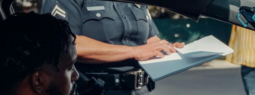 Driver sitting in a car while a police officer writes a citation outside the window.