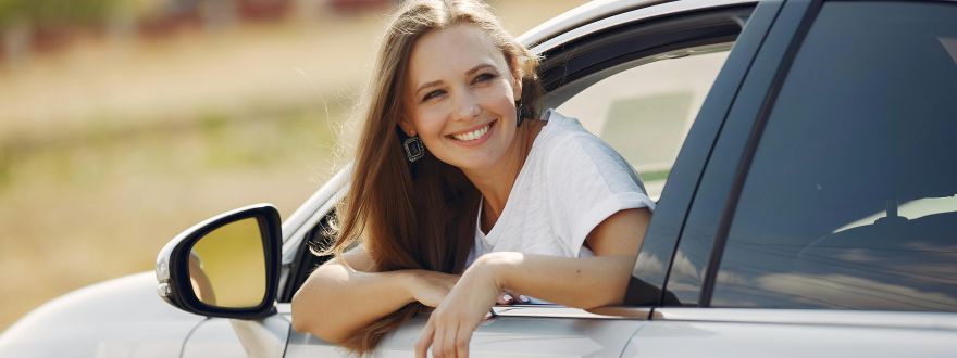 A woman smiles as she leans out of the drivers side window of a car.