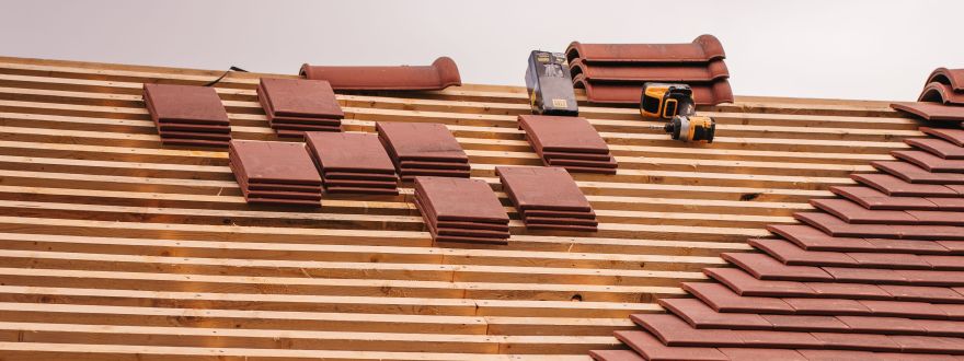 Photo showing a tile roof halfway completed and under construction with stacks of uninstalled tiles.