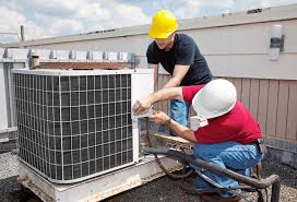 Two people working on an AC unit. Both are wearing hard hats. 