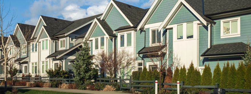 Row of modern townhomes and condos with peaked roofs under a bright blue sky