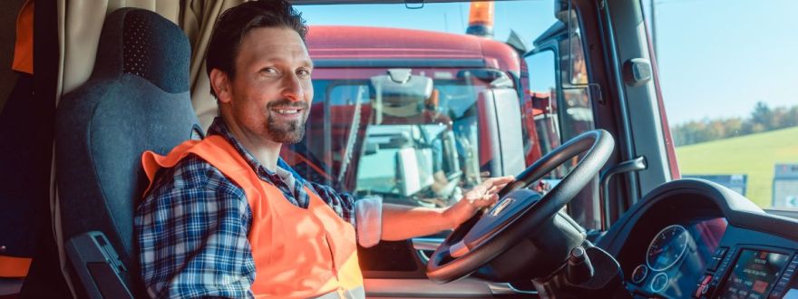 A truck driver is sitting and smiling is his truck