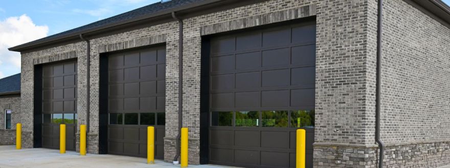 A brick commercial property with three large closed garage doors and yellow bollards under a partly cloudy sky.