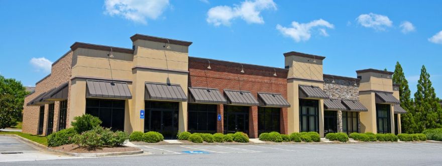A modern strip mall with beige and brown brick facade, large windows.