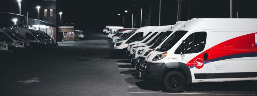 A fleet of commercial delivery vans parked in a lot at night under streetlights.