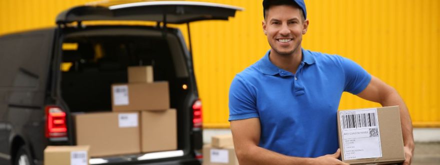 A smiling delivery driver holding a package in front of a van loaded with parcels, standing against a bright yellow background.