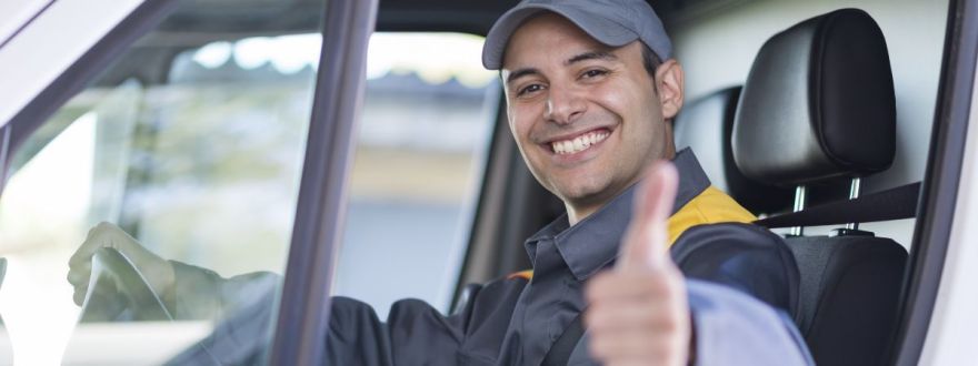 Smiling commercial driver in uniform tipping his cap while seated in a work vehicle.
