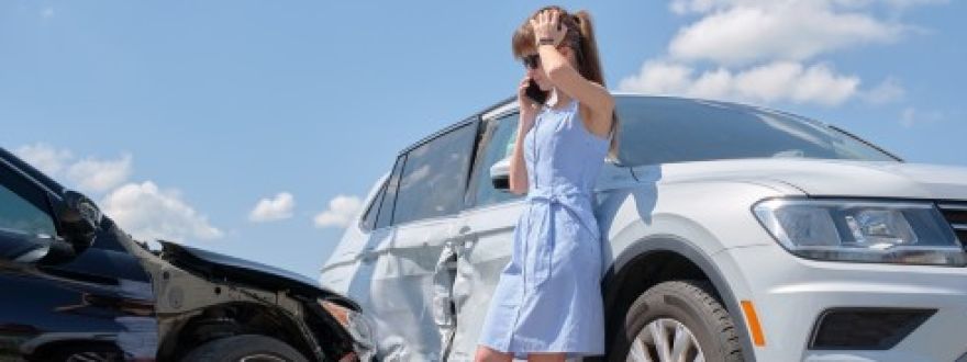 Woman on phone beside two cars after a collision, looking stressed.