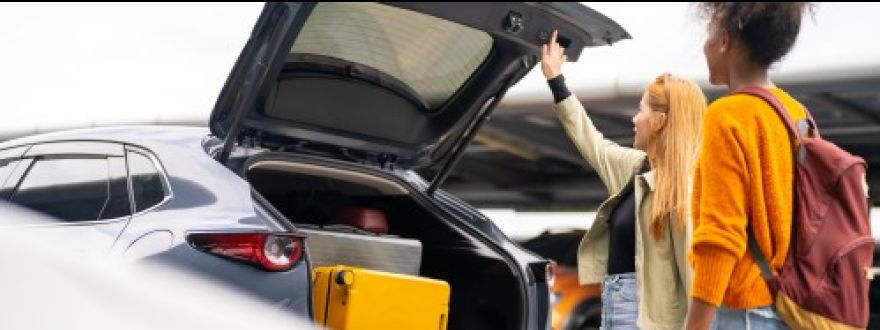 Two people loading luggage into the open trunk of a dark-colored SUV.