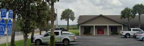 Image of an Insurance office with a red door, a parking lot is in the foreground with vehicles.