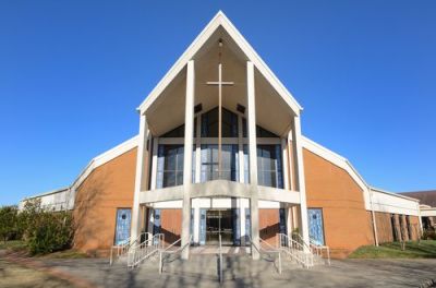Modern brick and white church building with a large A-frame entrance and cross against a clear blue sky.