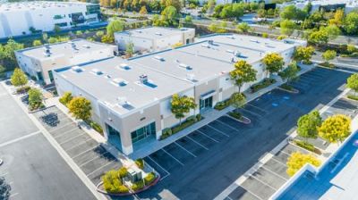 Aerial view of a modern business park with beige commercial buildings and parking lots on a sunny day.