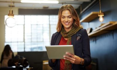 Woman entrepreneur smiles while using a tablet in her modern boutique or workshop setting.