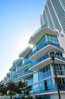 A low-angle shot of a modern white building with blue glass balconies against a bright blue sky; a street lamp is in the foreground.