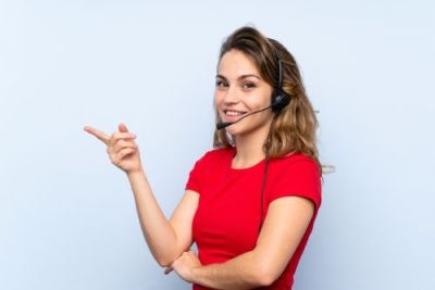 Friendly customer support agent with a headset smiling and pointing left against a light blue background.