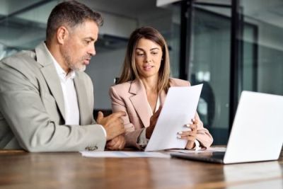 Two colleagues review paperwork together in a professional office setting.