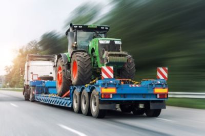 Truck hauling green tractor on blue flatbed trailer on highway at dawn/dusk; motion blur.