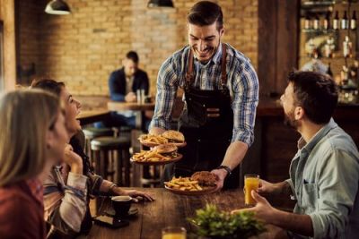 Smiling waiter serves burgers and fries to happy customers at a restaurant table.
